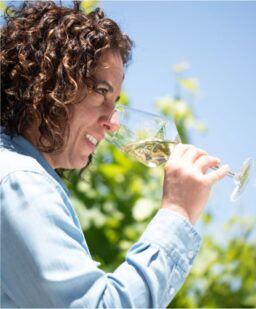 Seaglass winemaker Christine Morrison noses a glass of white wine standing in a sunny vineyard
