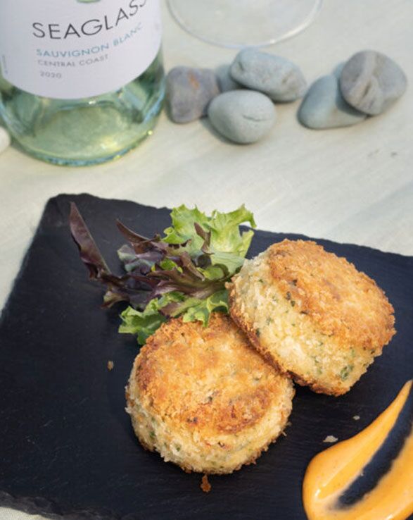 Crab Cakes lie on a plate next to a chilled bottle of Seaglass Central Coast Sauvignon Blanc