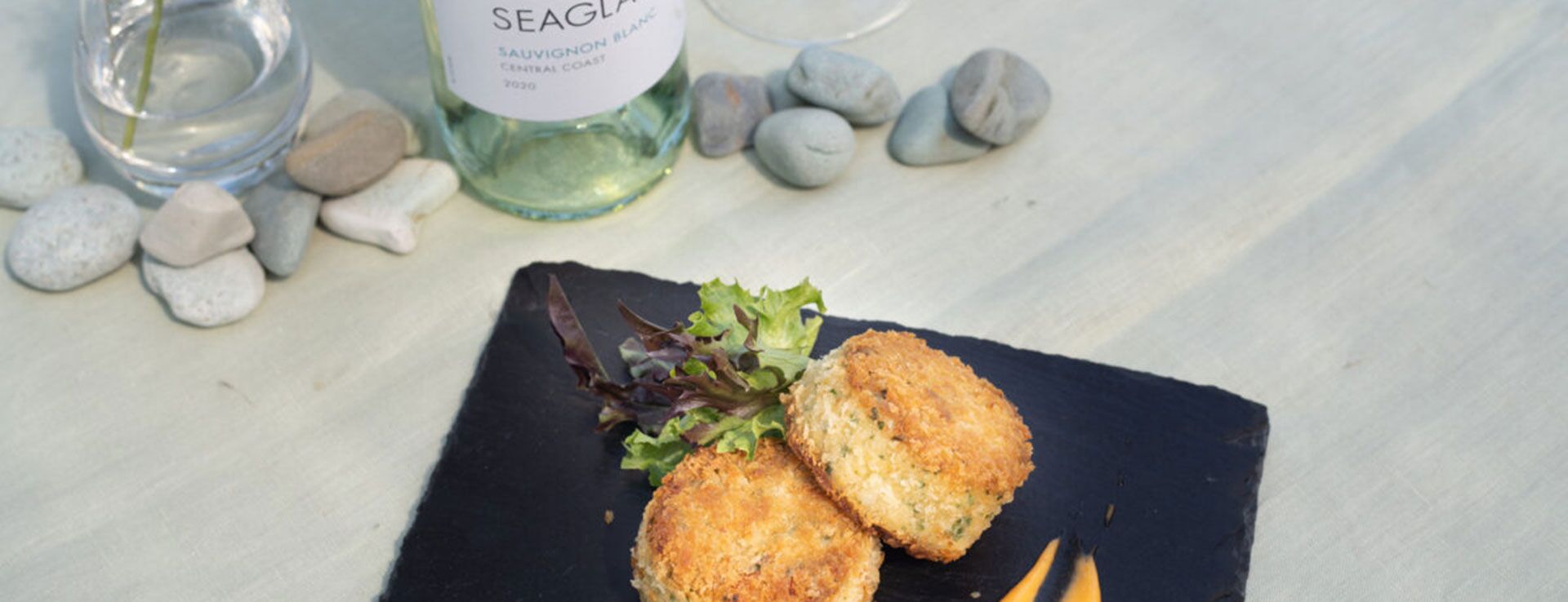 Crab Cakes lie on a plate next to a chilled bottle of Seaglass Central Coast Sauvignon Blanc