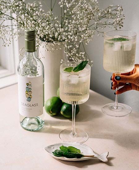 Two cocktails next to a bottle of SEAGLASS Pinot Grigio on a table next to a sunny window