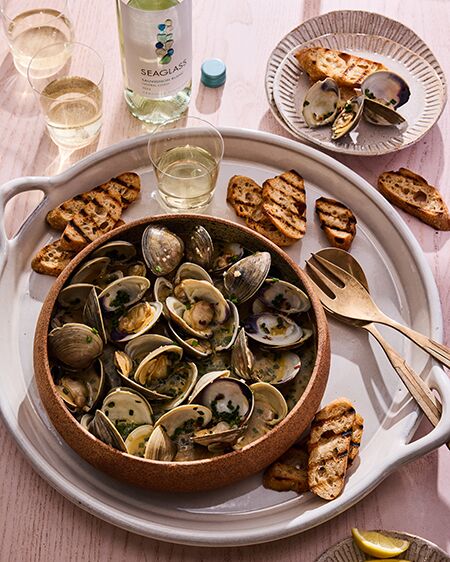 A bowl of Steamed Clams in White Wine + Herbs with a glass and bottle of SEAGLASS Sauvignon Blanc