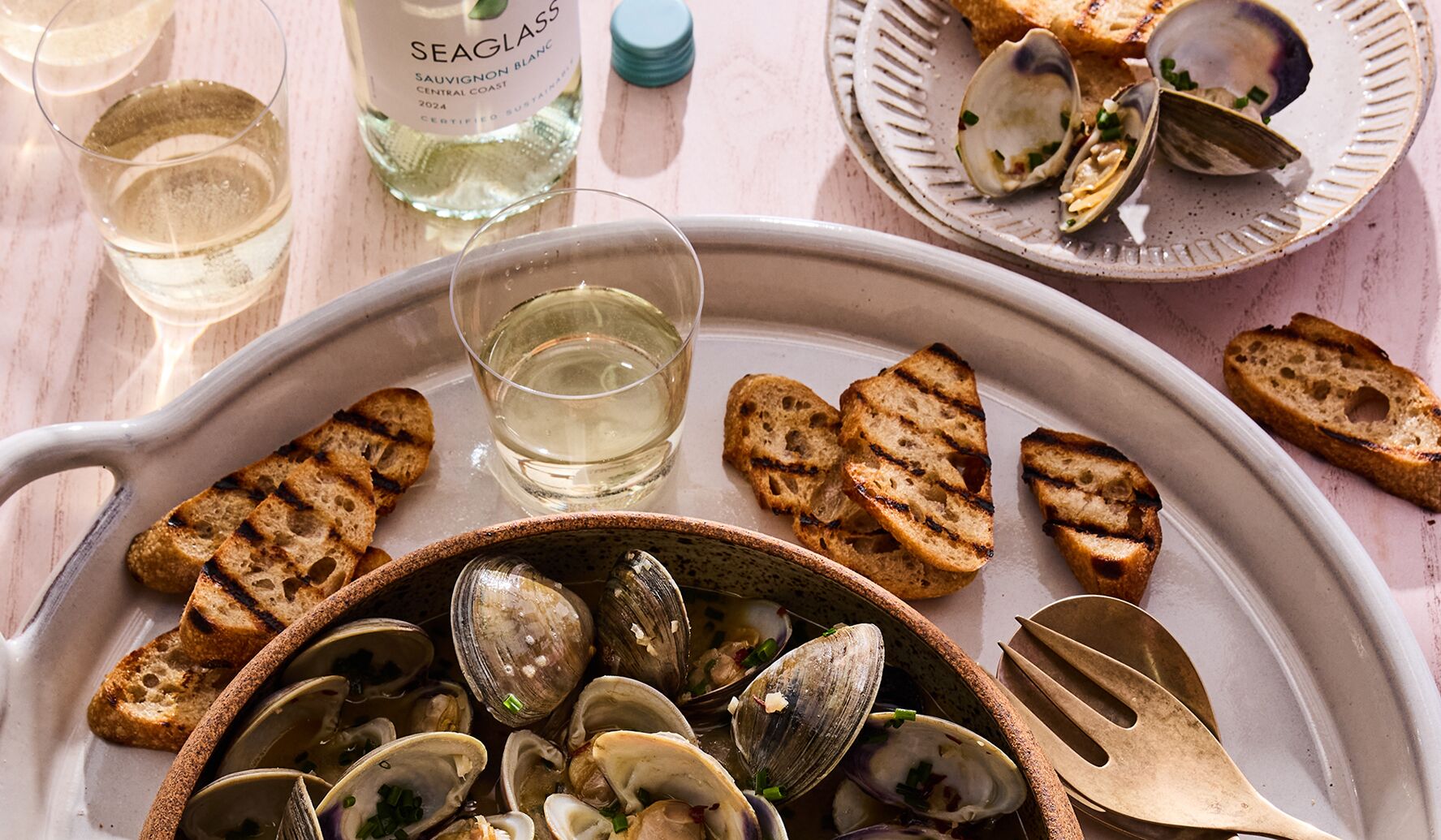 A bowl of Steamed Clams in White Wine + Herbs with a glass and bottle of SEAGLASS Sauvignon Blanc