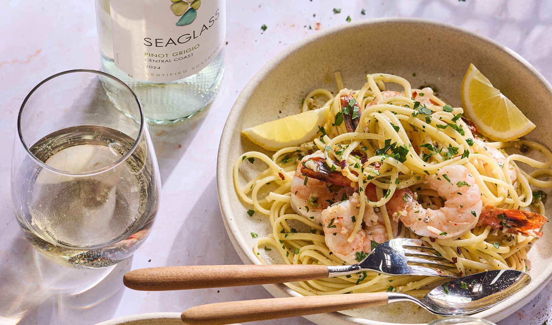 A bowl of garlic shrimp scampi with lemon and a glass of SEAGLASS Pinot Grigio